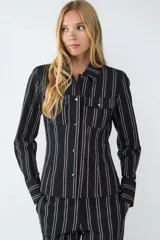 Camisa de manga larga confeccionada en popelina de algodón, con diseño de rayas verticales en tonos oscuros. Presenta cuello clásico, cierre frontal con botones metálicos y dos bolsillos frontales con solapa.