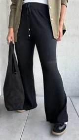 Pantalón de tejido de punto acanalado en color negro, con corte recto y ligeramente acampanado en el bajo. Presenta una cintura elástica con cordón ajustable y terminaciones con herrajes metálicos.
