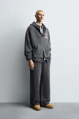 Pantalón jogger de corte wide fit confeccionado en tejido de algodón con interior de rizo. Presenta cintura elástica ajustable con cordón, bandas laterales decorativas, bolsillos laterales y un bolsillo trasero de plastrón. El acabado presenta un efecto lavado que le otorga una apariencia única.