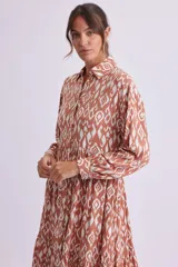 Vestido camisero midi color marrón con estampado geométrico en blanco, de corte recto, con cuello camisero, abotonadura frontal y mangas largas con puños abotonados.