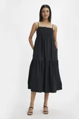 Vestido midi de color negro con tirantes finos, escote cuadrado y cuerpo con detalle de alforzas y botones frontales. Presenta una falda amplia con corte escalonado y bolsillos laterales.