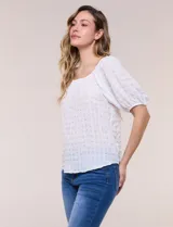 Blusa blanca de tela texturada y silueta fluida, con escote en U y frunces. Cuenta con mangas cortas abullonadas con elástico en los puños y ruedo redondeado.