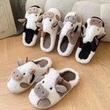 Pantuflas de peluche con diseño de vaca, confeccionadas en piel sintética suave. Cuentan con suela de goma antideslizante y diseño abierto en el talón.