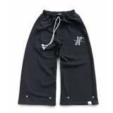 Pantalón de jogging negro de corte baggy, confeccionado en algodón. Presenta cintura elástica con cordón largo ajustable, bordado de logo en la parte superior y botones metálicos en la botamanga que permiten ajustar el ancho del ruedo.