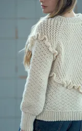Sweater tejido a crochet en lana merino color crudo, con cuello redondo y manga larga. Presenta una trenza diagonal con volados en el frente.