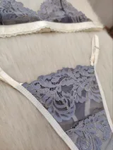Conjunto de lencería compuesto por un corpiño triangular y una bombacha tipo tanga, confeccionados en encaje gris con detalles de terminaciones en color champagne.