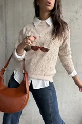 Sweater de punto color beige con diseño floral en relieve, cuello redondo y mangas largas. Presenta puños y ruedo acanalados.
