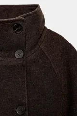 Abrigo largo confeccionado en hilatura con lana, de corte recto y diseño estructurado. Presenta cuello subido, manga larga, bolsillos delanteros de vivo y cierre frontal con botones. Incluye un cinturón del mismo tejido para ajustar a la cintura y abertura en la espalda.