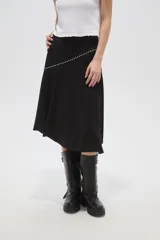 Falda midi negra de corte asimétrico, con detalle de costura diagonal decorada con pequeñas tachas metálicas.