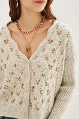 Cardigan de punto color beige con diseño de flores bordadas, escote en V, cierre frontal con botones y mangas largas con puños acanalados.