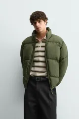 Cazadora acolchada tipo puffer de corte relajado, color verde militar. Presenta cuello subido, cierre frontal con cremallera, bolsillos laterales con cierre y puños elásticos.