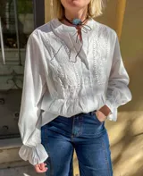 Blusa blanca de manga larga con detalles de bordado floral y calados en el frente. Presenta cuello mao con cierre frontal de botones y puños con volados.