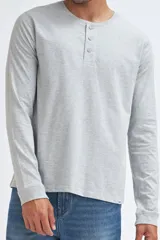 Remera de manga larga en color gris claro melange, confeccionada en tejido de punto suave. Presenta un cuello redondo con una pequeña abertura frontal cerrada por tres botones.