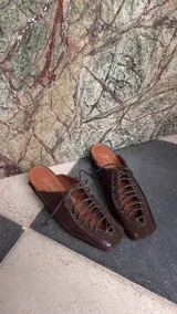 Zapatos destalonados marrones de tacón bajo, estilo mules, con diseño acordonado en el empeine, punta cuadrada y combinación de texturas en cuero y gamuza.