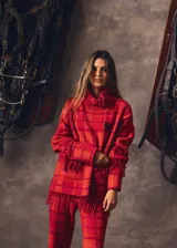 Sweater oversize de lana natural con estampado cuadrillé en tonos azul, verde y rojo. Presenta cuello alto, mangas largas y detalles de flecos torneados en el cuello, puños y dobladillo.