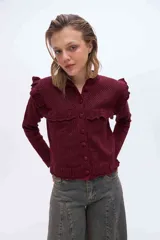 Saco de punto color bordó con brillo sutil, mangas largas y cierre frontal con botones forrados. Presenta un canesú destacado con volados tejidos, delicados calados y terminaciones onduladas.