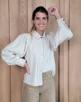 Camisa de color arena con mangas abullonadas, puños anchos con botones y cuello clásico. Presenta un diseño de corte recto con costuras visibles y cierre frontal oculto.
