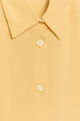 Camisa oversize color amarillo pastel, con cuello solapa, manga larga con puño y cierre frontal con botones.