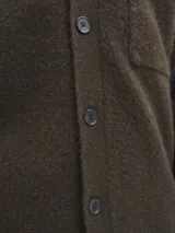 Cardigan de punto color marrón oscuro, con cuello tipo polo, cierre frontal con botones y un bolsillo aplicado en el pecho. Presenta mangas largas con hombros caídos y puños acanalados.