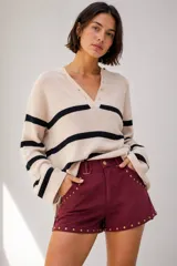 Short de tiro medio con efecto gamuza en color bordó, decorado con tachas metálicas doradas en los bordes y bolsillos. Cuenta con presillas para cinturón y cierre frontal.