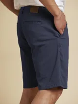 Bermuda de gabardina azul marino con bolsillos laterales y traseros, cierre frontal con botón y cremallera, y trabillas para cinturón.