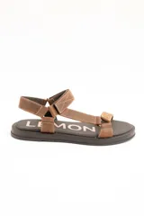 Sandalias planas de cuero marrón con tiras regulables mediante velcro y suela negra.