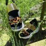 Sandalias con plataforma blanca, tiras de cuero con estampado animal print y tira trasera de cuero negro con hebilla dorada.