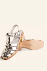 Sandalia plateada de cuero con tiras entrecruzadas, taco de madera y hebilla lateral.