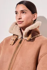 Campera gamulan color rosa con interior de piel sintética color crema, cierre frontal con cremallera y hebillas en el cuello. Corte oversize.