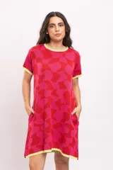 Vestido corto tejido de punto con diseño geométrico abstracto en tonos rojo y fucsia, cuello redondo, mangas cortas y bolsillos laterales, con detalles en amarillo en el cuello, puños y ruedo.