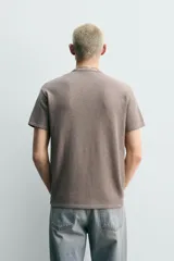 Remera de punto de algodón color gris topo, con efecto lavado, cuello redondo y manga corta. Cuenta con aplicación de parches con texto desgastado en el frente.