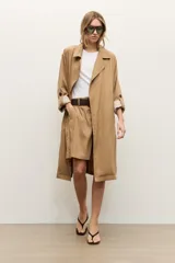 Trench de lyocell color beige con solapas amplias, cierre cruzado con botones, bolsillos laterales y mangas largas con presillas en los puños que permiten ajustarlas.