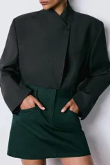 Falda mini de tiro bajo confeccionada en sarga de algodón, con diseño de cinco bolsillos, trabillas en la cintura y cierre frontal con cremallera y ganchos metálicos.