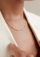 Collar de acero dorado con cadena fina y pequeñas cuentas esféricas distribuidas a lo largo de la pieza.