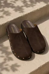 Zueco de gamuza color marrón, con costura vertical central y tachas metálicas doradas alrededor de la suela.