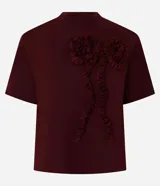 Remera femenina de manga corta color bordó, con cuello redondo y una aplicación figurativa en forma de lazo en la parte delantera, hecha en tejido fruncido que crea relieve. Confeccionada en algodón certificado BCI.