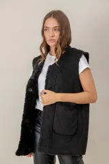 Chaleco largo de gamuza sintética color negro, con interior de piel sintética (faux fur) y cierre frontal con botones. Presenta bolsillos frontales amplios y diseño reversible.