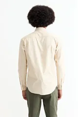 Camisa de manga larga color crema, con cuello camisero y botones frontales. Corte ajustado.