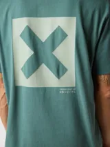 Camiseta de manga corta color verde azulado, corte holgado, con un pequeño estampado cuadrado con una 'X' en el pecho.