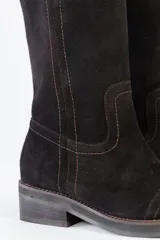 Bota de caña media confeccionada en cuero gamuzado color negro, con costuras a la vista en tono contrastante. Presenta un detalle de cadena metálica plateada con dijes colgantes en forma de llaves y candados alrededor del tobillo. Cuenta con un taco cuadrado de madera y suela de goma.