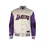 Campera bomber de algodón color crema con mangas de cuero sintético color violeta. Tiene el logo de Los Angeles Lakers bordado en el pecho y parches en los codos.