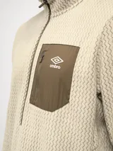 Buzo de entrenamiento Umbro con medio cierre frontal, cuello alto y bolsillo en el pecho de nylon con cierre. Presenta una textura sutil en el tejido y logo de la marca estampado en el bolsillo.