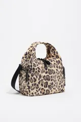 Bolso bandolera de estructura blanda marca Bimba y Lola, confeccionado en nylon con estampado animal print de leopardo. Presenta doble asa de mano integrada, correa de tejido negra regulable y extraíble, bolsillos laterales con cierre y logo metálico de la marca en el frente.