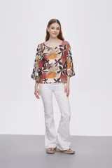 Blusa estampada con flores en tonos marrones, naranjas y negros, con mangas 3/4 acampanadas y cuello redondo.