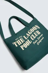 Bolso tipo shopper de algodón en color verde oscuro, con diseño de estampado tipográfico en color crema en el frente. Cuenta con dos asas de mano y cierre magnético.