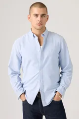 Camisa celeste de manga larga con cuello abotonado y cierre frontal de botones. Confeccionada en algodón con sutil bordado en el pecho.