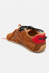 Championes de gamuza color marrón con detalles en cuero liso del mismo tono. Presentan cordones bicolores en naranja y negro, suela de goma plana y un detalle en color rojo en la parte trasera del talón.