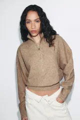 Jersey de punto melange color beige, con cuello subido, cierre frontal con cremallera y manga larga con hombros caídos.