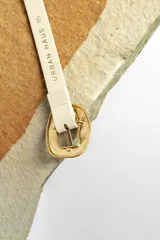 Cinturón color crema con hebilla cuadrada dorada con diseño irregular.