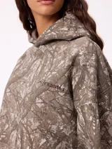 Canguro con capucha de corte holgado, estampado con diseño de ramas en tonos marrones y beige. Presenta bolsillo frontal tipo canguro, puños y ruedo en tejido rib elástico, y logo de la marca bordado en el pecho.